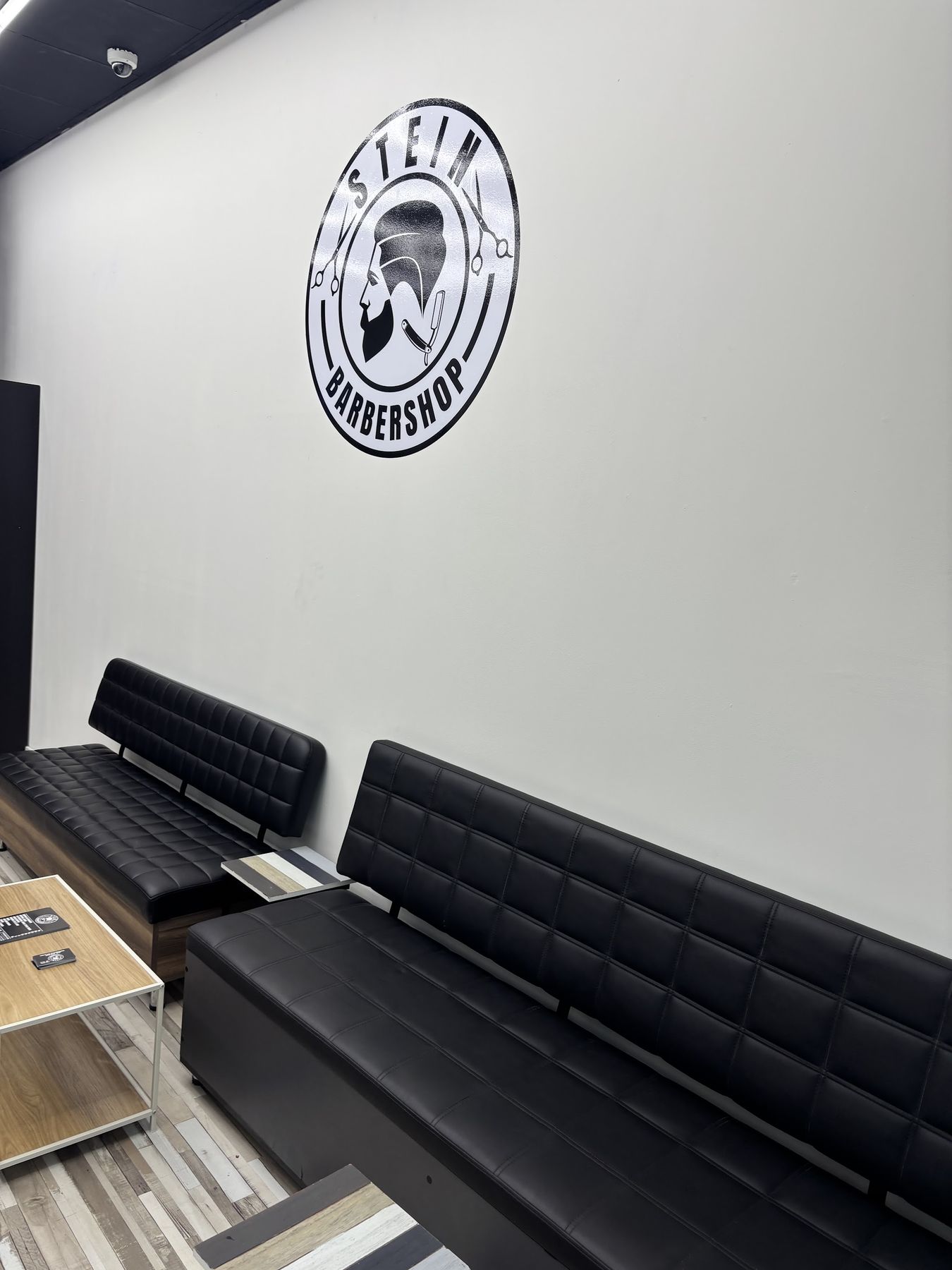 Wachtruimte met zwarte banken en het ronde Stein Barbershop-logo op de muur